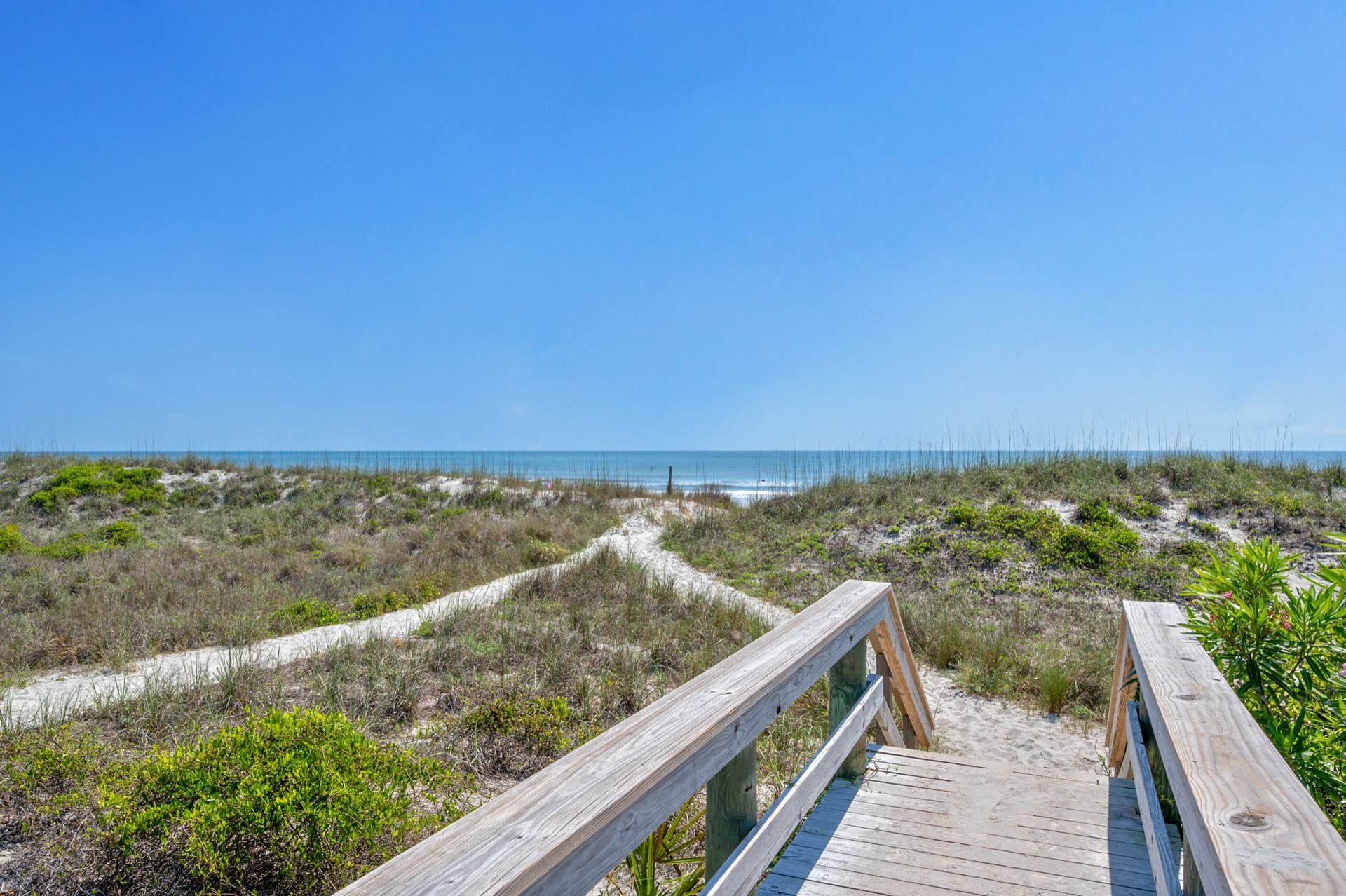 Wooden boardwalk stairs leading over dunes to the ocean under a clear blue sky