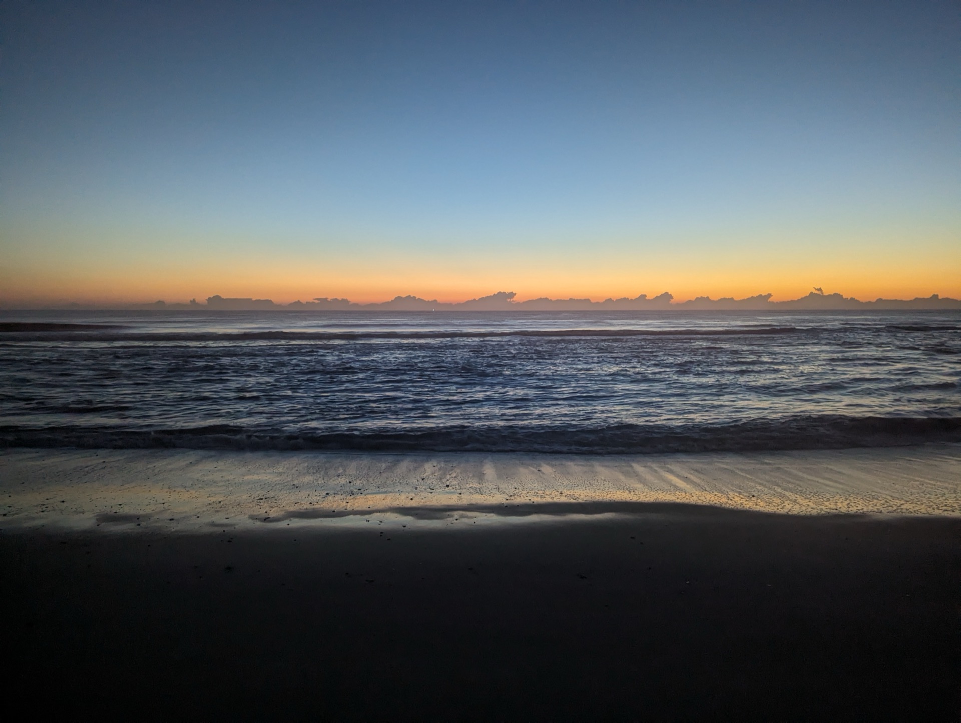 Pre-dawn light over the Atlantic with gentle waves washing onto packed sand at low tide