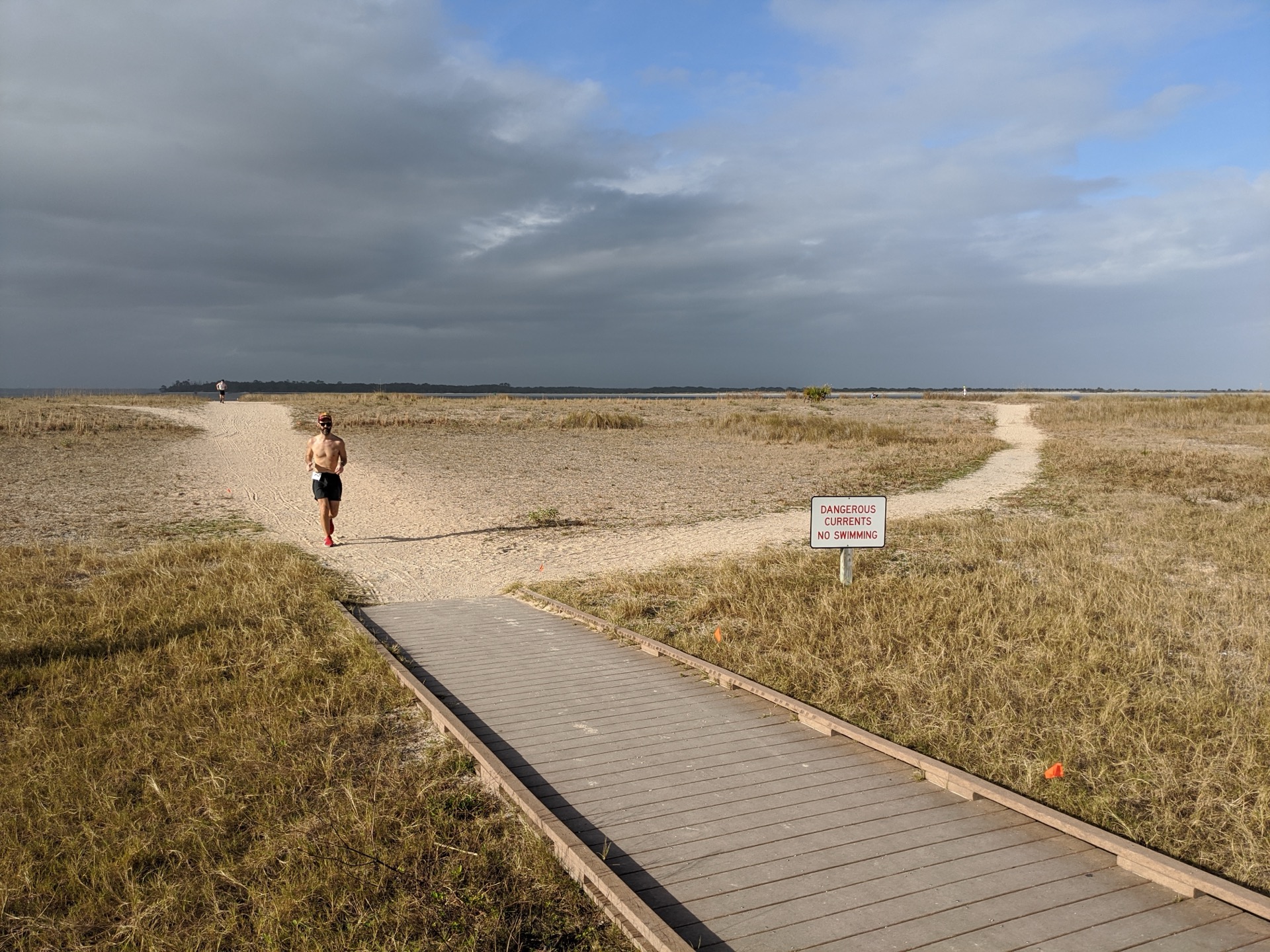 Runner on a boardwalk heading toward the beach at Fort Clinch with dramatic clouds overhead